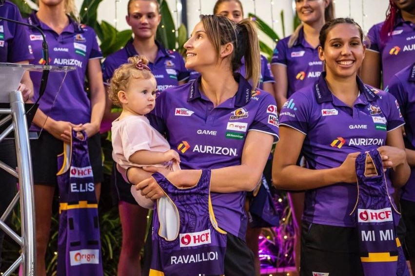 El centro de Queensland Firebirds, Kim Ravaillion, sosteniendo a su hija en una presentación de jersey