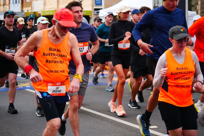 An older man in a high vis shirt running in a pack of competitors along a Ballarat street.
