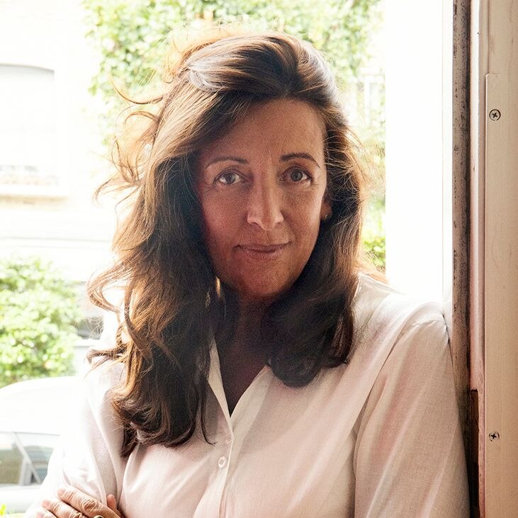 Author Louise Doughty wearing cream top, pictured with her arms crossed leaning against a door. She has long brown hair