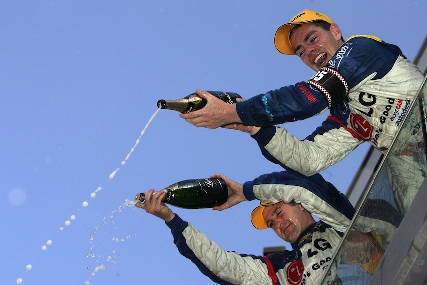 Two male Supercars drivers spray sparkling wine over a crowd.