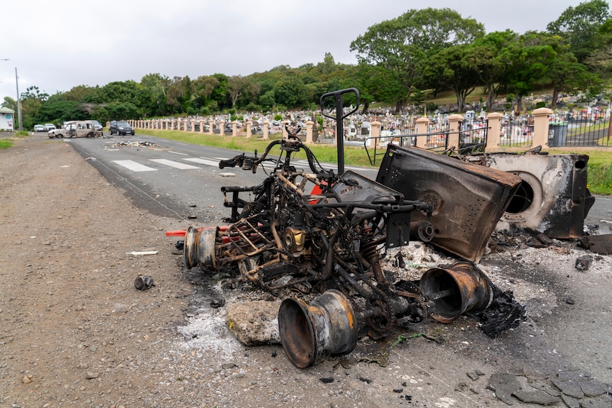 The charred skeleton of a car sits on a road.