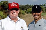 Donald Trump stands in between Jack Nicklaus and Tiger Woods on a golf course. Mr Trump is wearing his red USA cap.