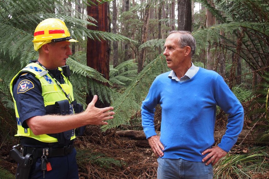 A police officer in a hi vis top speaks to former Greens leader Bob Brown in a forest.