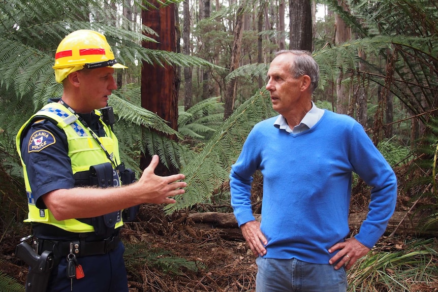 A police officer in a hi vis top speaks to former Greens leader Bob Brown in a forest.