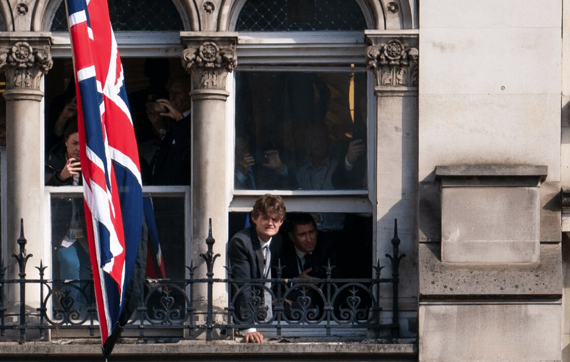 People perched in a high window look down as the Queen's coffin passes by.