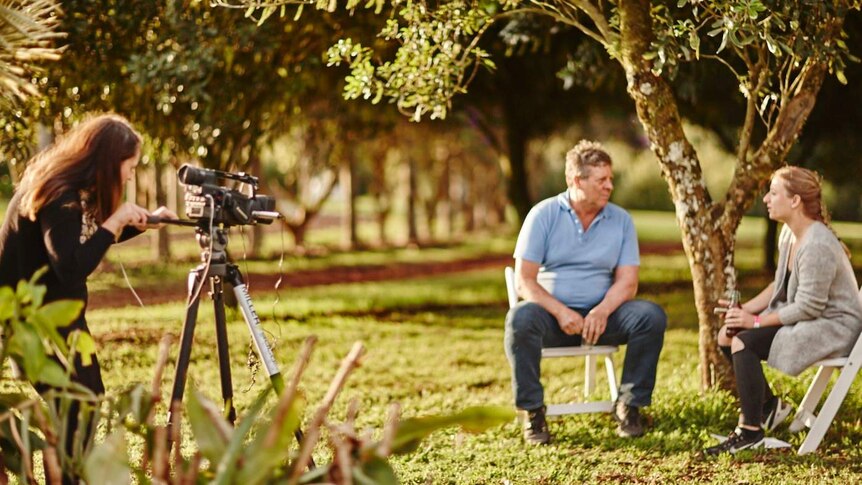 Reporter films an international delegate speaking to a macadamia farmer.