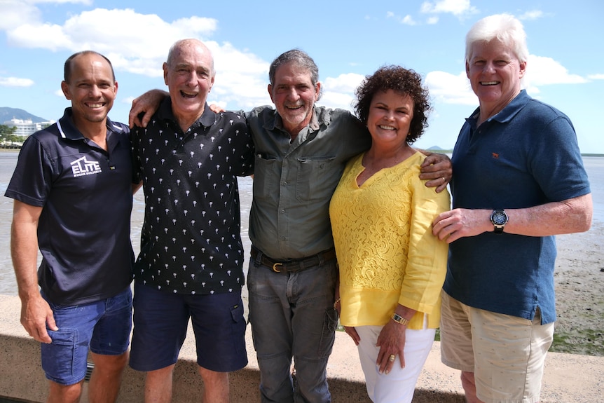 Photo of four men and a women smiling on the foreshore