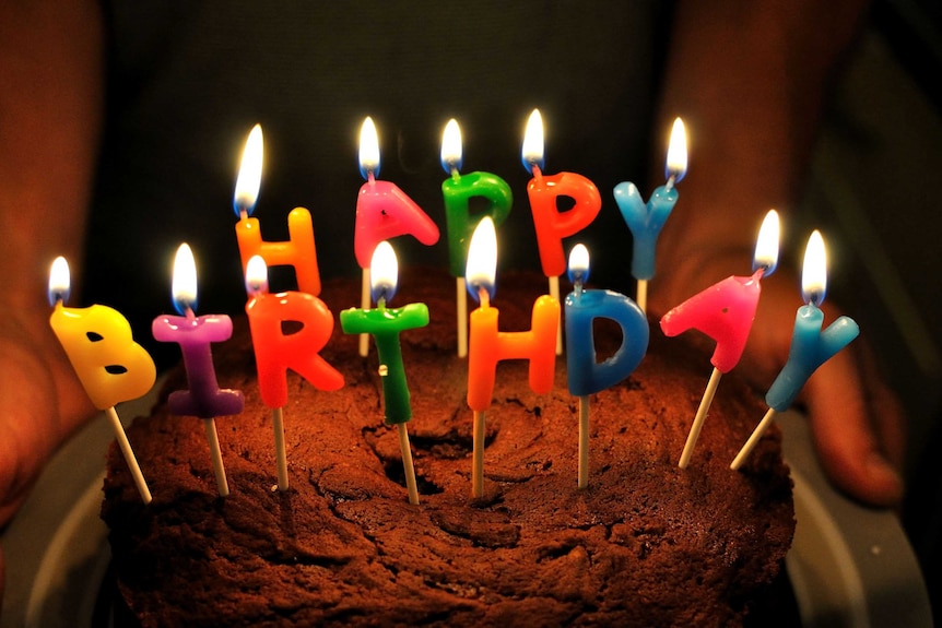 A chocolate cake with 'Happy Birthday' candles in it.