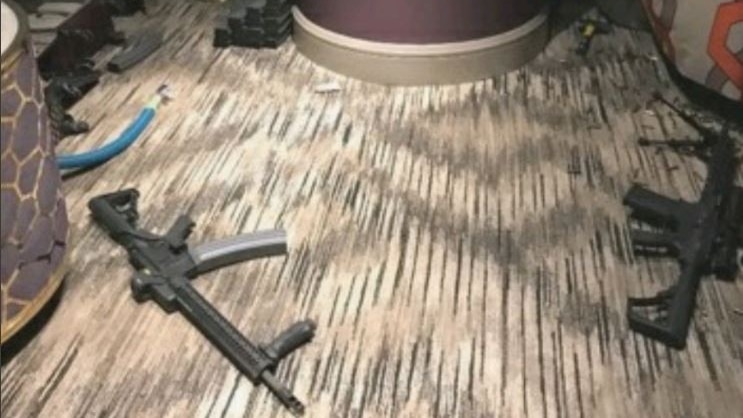 Two firearms are on brown carpet, with a hammer next to a pole in the background.