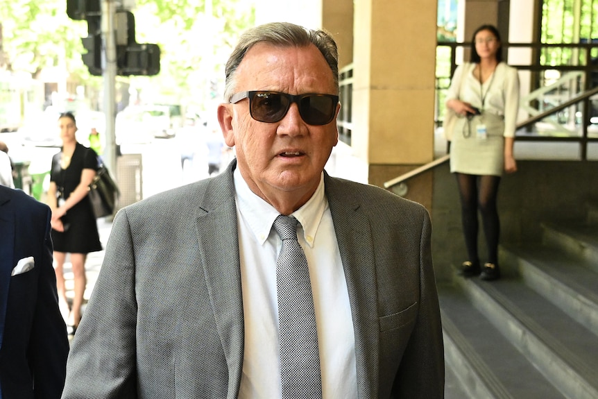Tim Mathieson wearing sunglasses and a grey suit as he walks into the Melbourne Magistrates' Court
