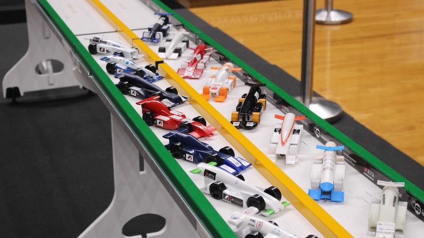 Different coloured model cars lined up on a track.