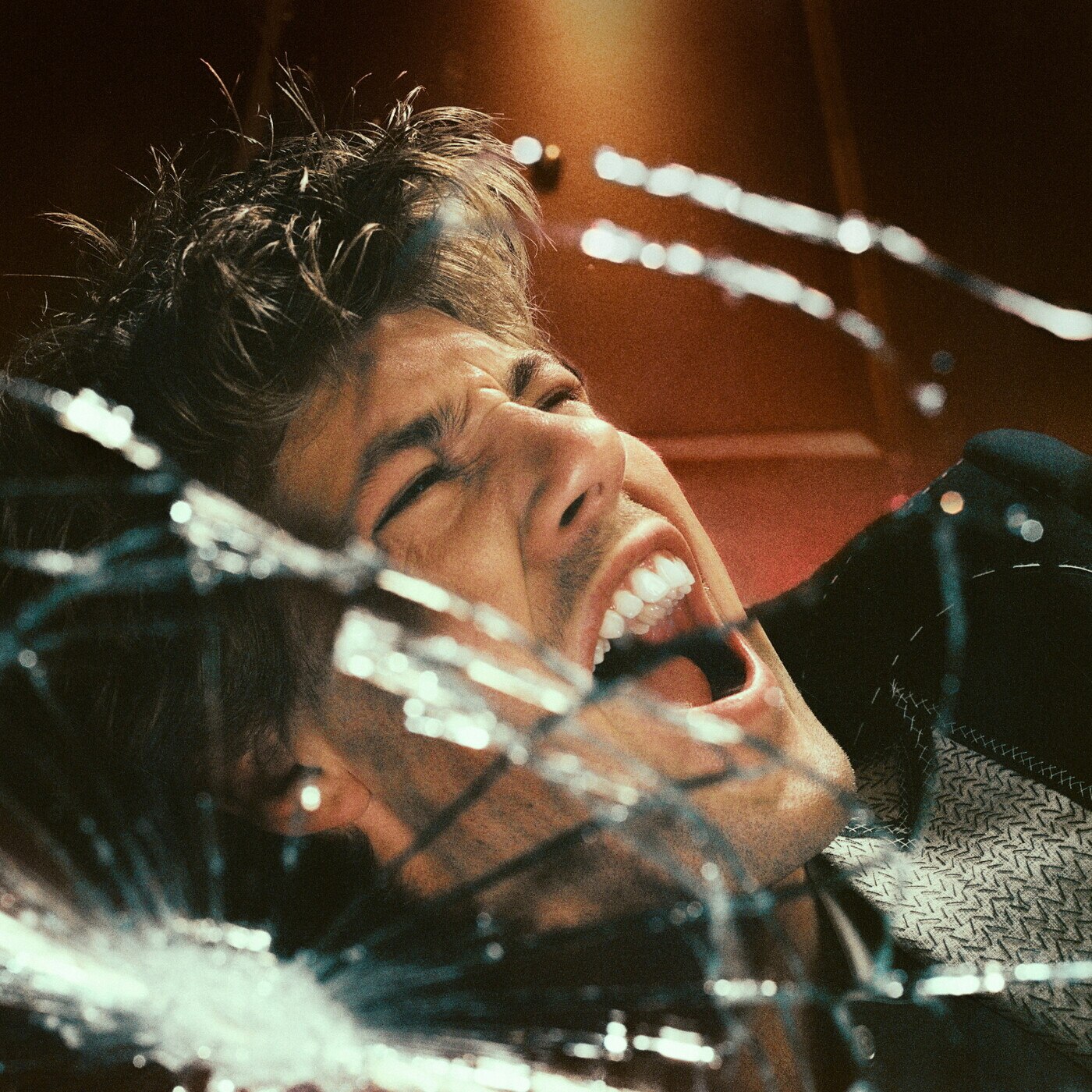 Man with brown hair screaming behind broken glass