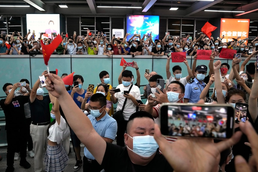 People crowded at an aiport in China with red Chinese flags and smartphones. 