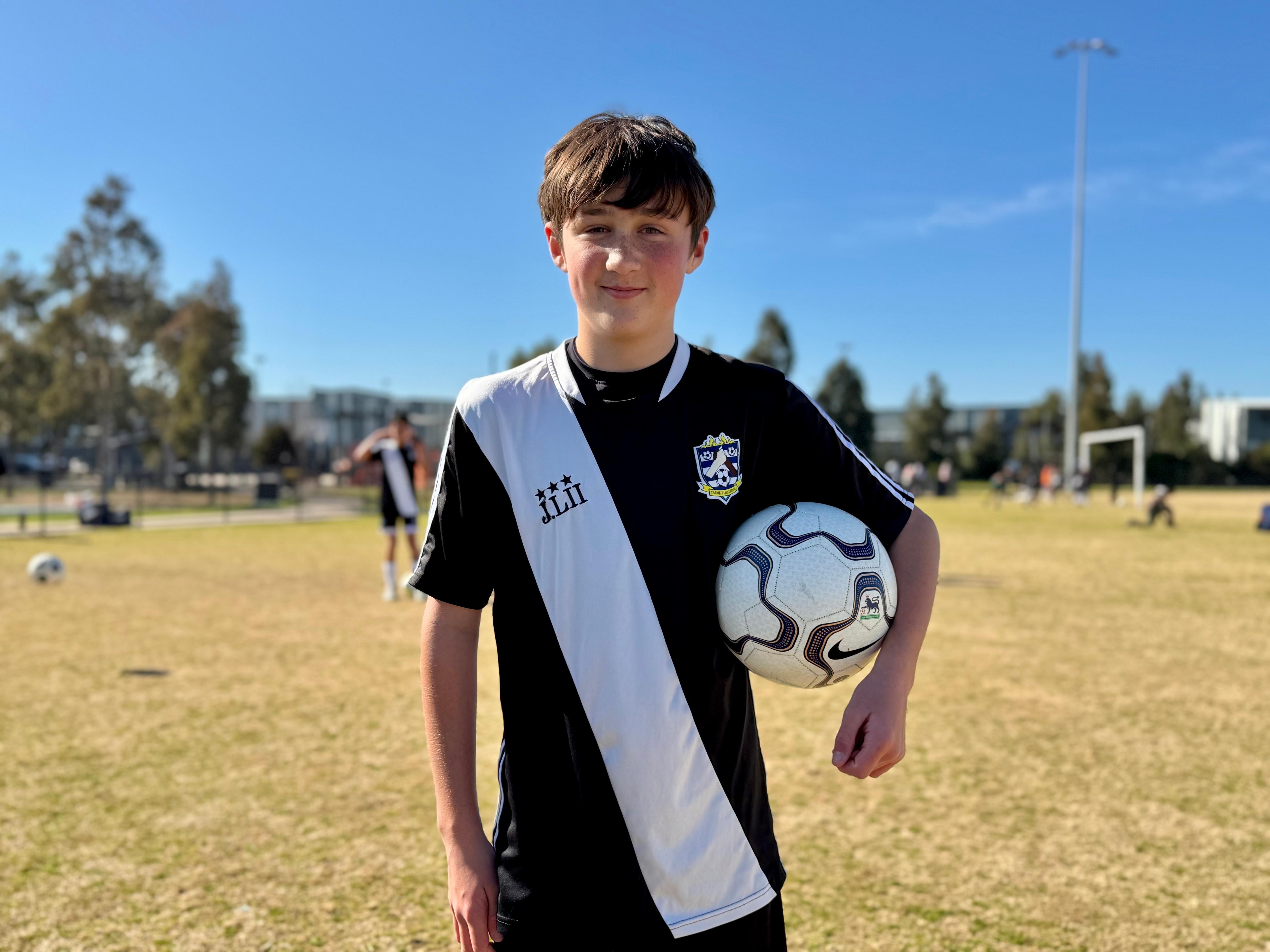 A boy holding a soccer ball smiles at the camera.