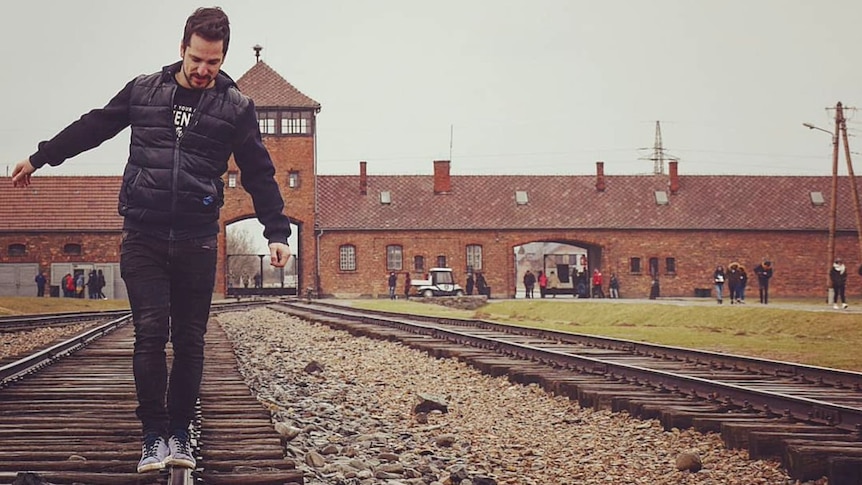 A man teeters as he walks on the railway that leads to the gatehouse of the Auschwitz concentration camp, which is behind him.