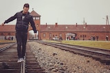 A man teeters as he walks on the railway that leads to the gatehouse of the Auschwitz concentration camp, which is behind him.