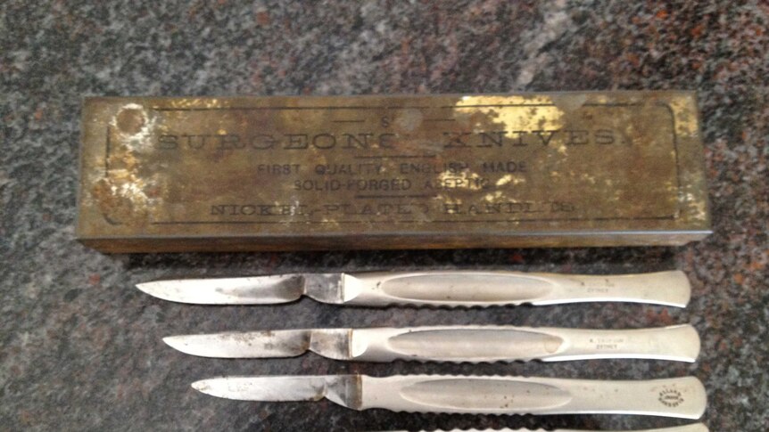 A worn box titled surgeon's knives with four knives underneath