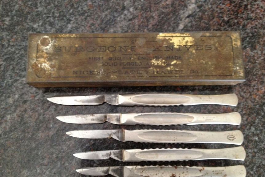 A worn box titled surgeon's knives with four knives underneath