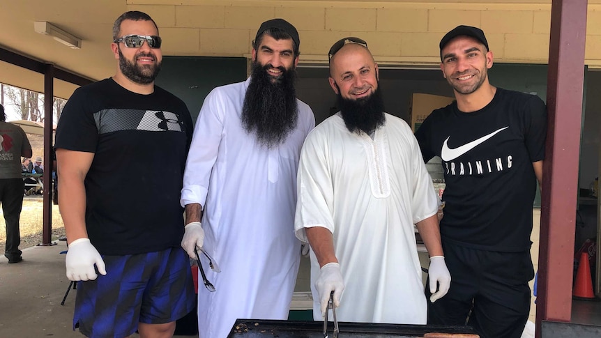 Four men cook sausages at a barbecue