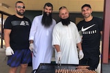 Four men cook sausages at a barbecue