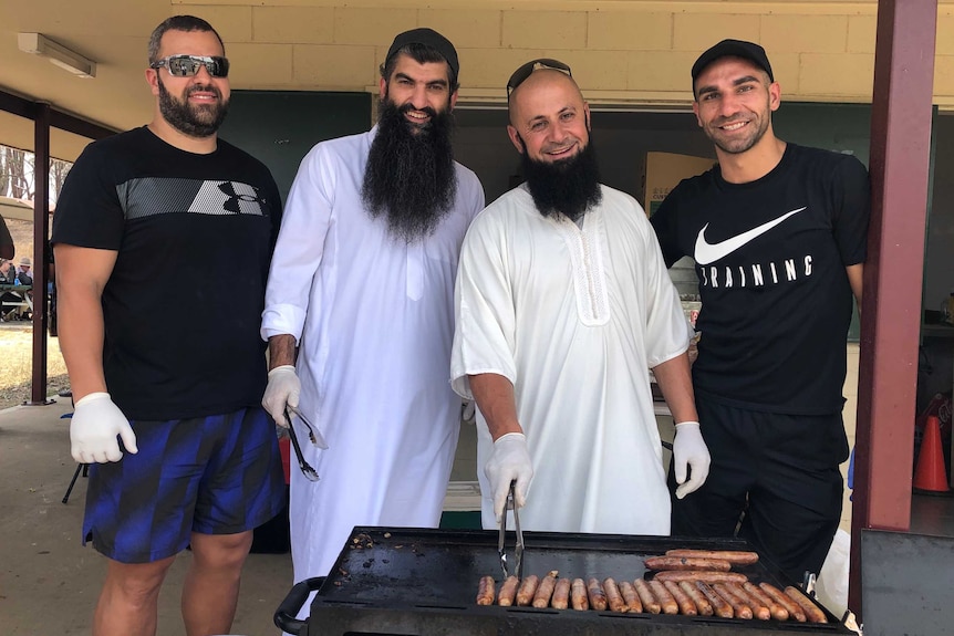 Four men cook sausages at a barbecue