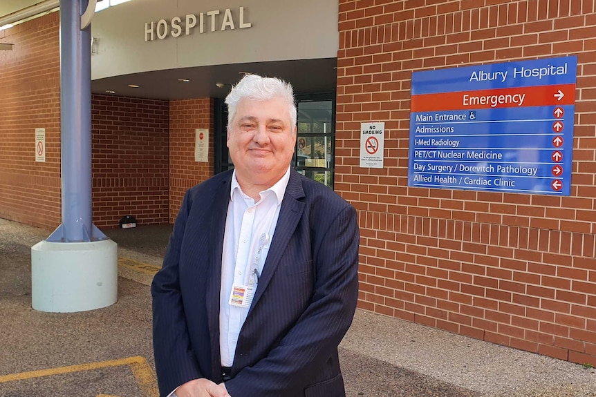 man with grey hair in suit stands at entrance to hospital