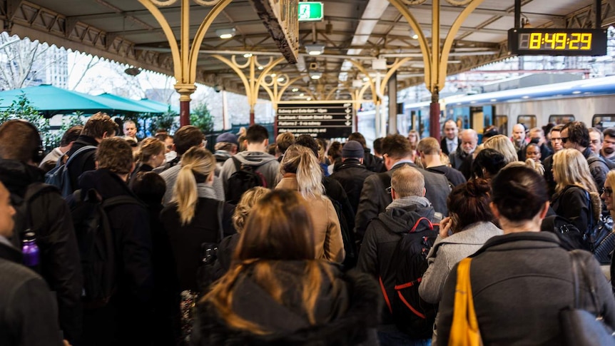 A large group of passengers walks along a platform at Flinders Street station.