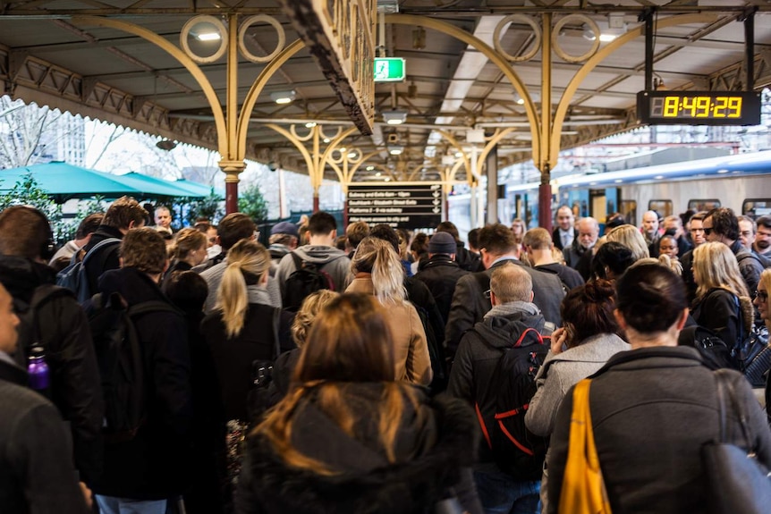 A large group of passengers walks along a platform at Flinders Street station.