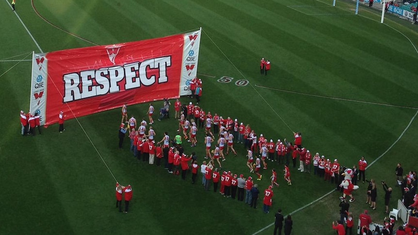 A big red banner reads 'RESPECT' as the Swans players stand on the oval at the MCG.