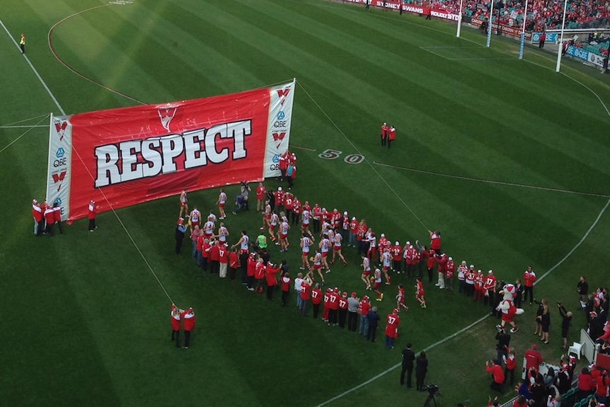 Sydney Swans players run onto the field at the Sydney Cricket Ground through a banner that reads "RESPECT".