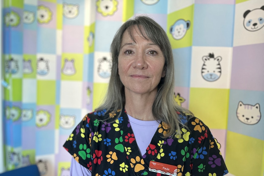 A woman in rainbow dogfoot patterned scrubs looking directly in to the camera. 