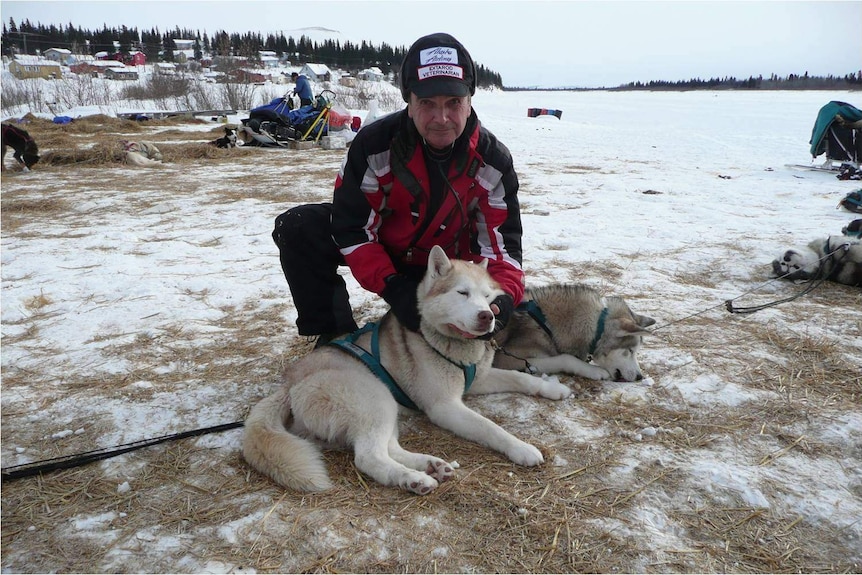 A man in parker and snow gear holding the head of a husky type dog on snow