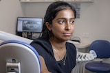 A woman sits on the dental chair in her office.