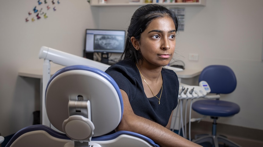 A woman sits on the dental chair in her office.