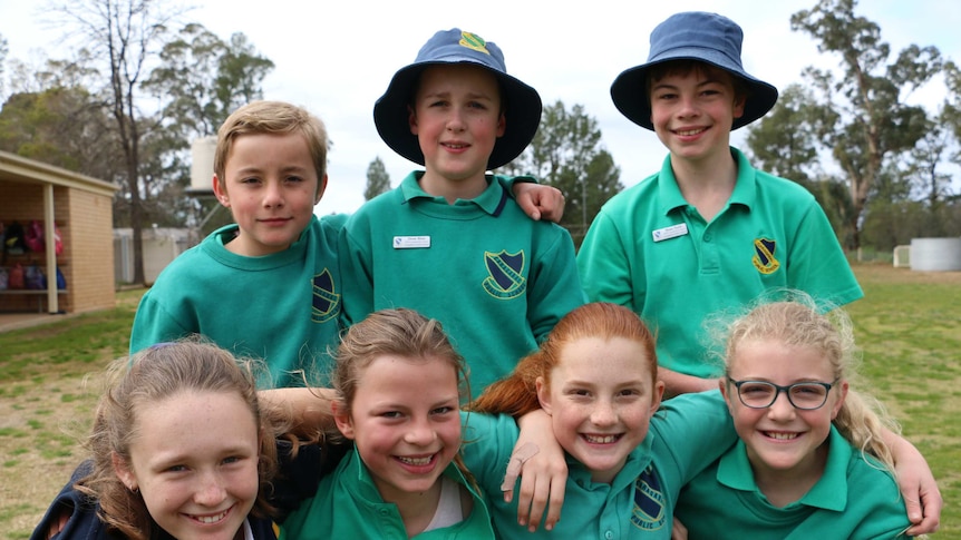 Seven school children wearing green uniforms smiling