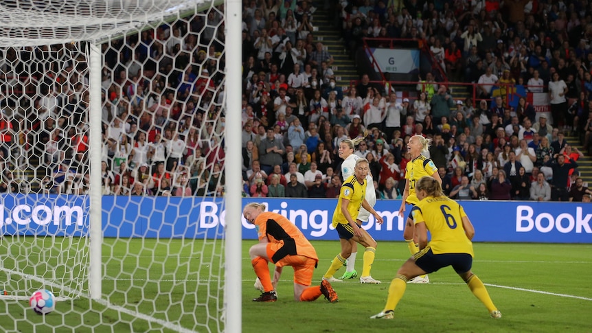 An England women's soccer player sees her backheeled shot go into the net as Swedish keeper and defenders look on.