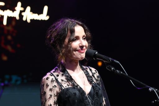An image of Tina Arena smiling behind a microphone