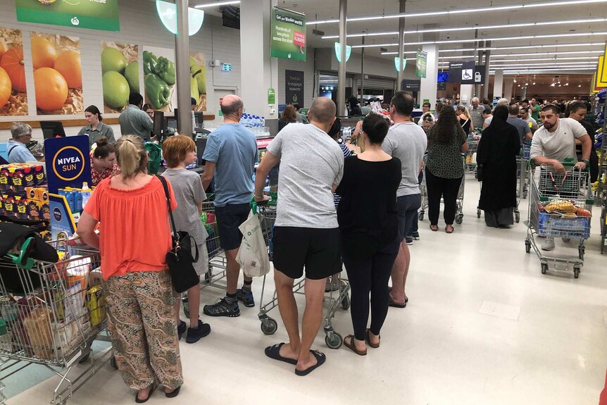 A long queues of customers with full trolleys at the checkouts inside a Woolworths store.