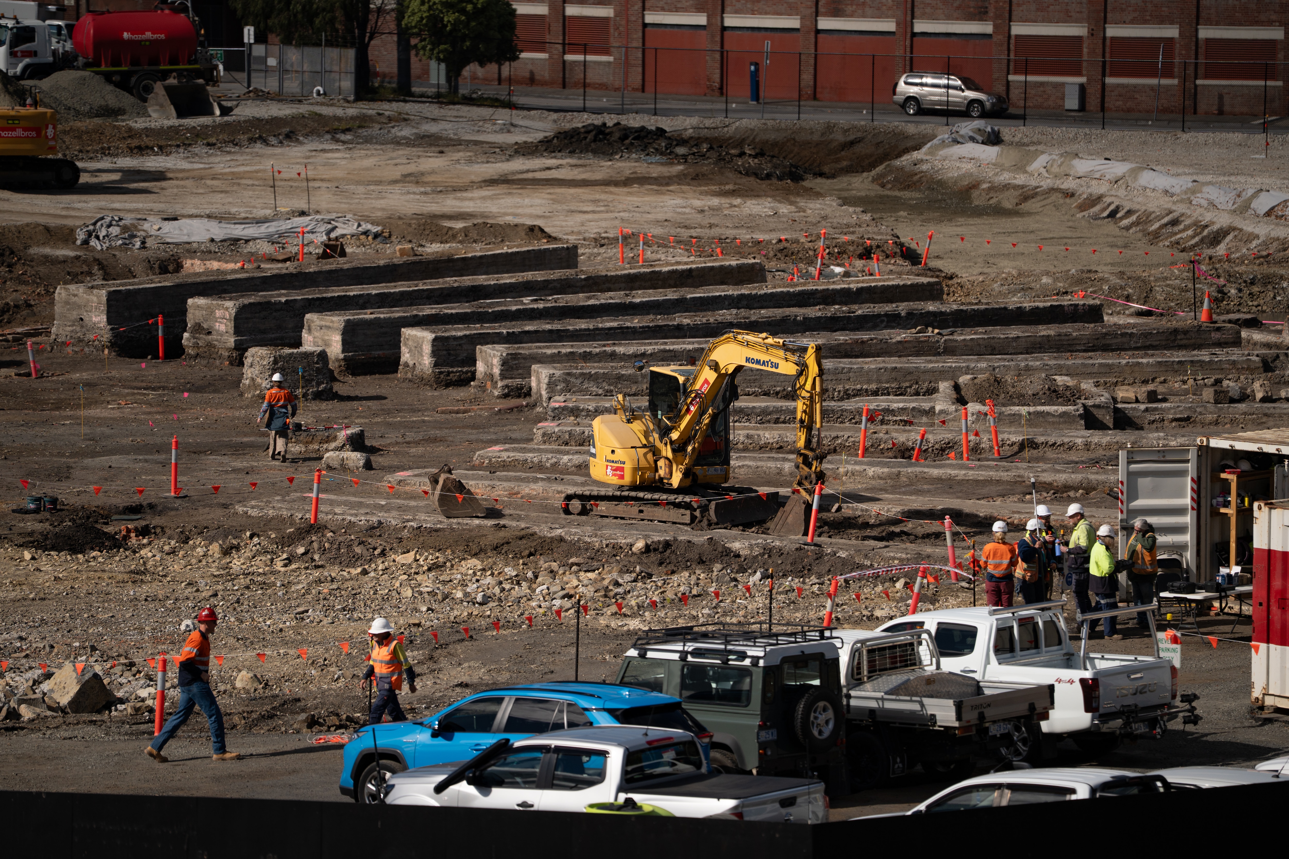 Exposed historical train turntable being dug up by yellow diggers, fluoro orange flags and workers in high vis stand around