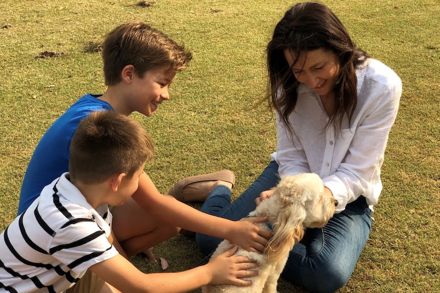 A woman and two boys pat a white fluffy dog