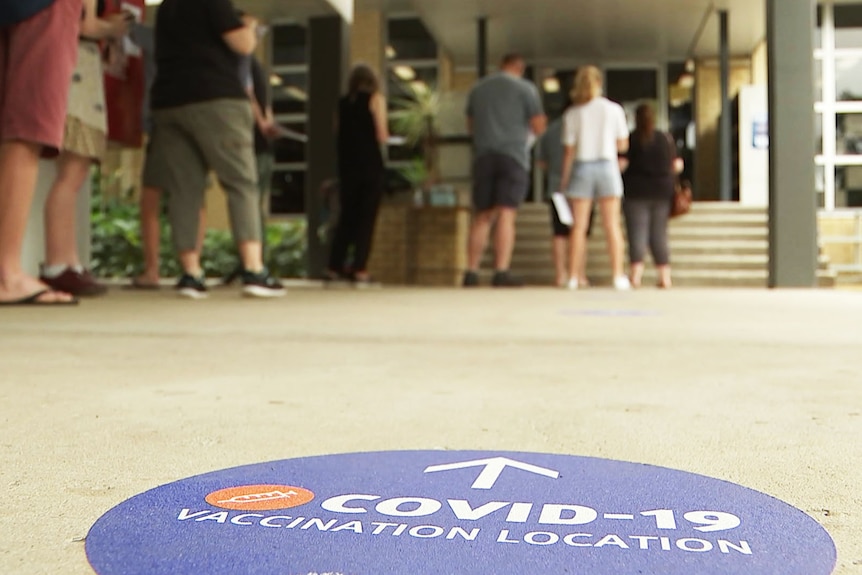 COVID-19 Vaccination Hub Dot on the ground behind a line of people in Brisbane's school.