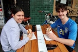 Two people smiling and eating sandwiches at a Melbourne cafe.