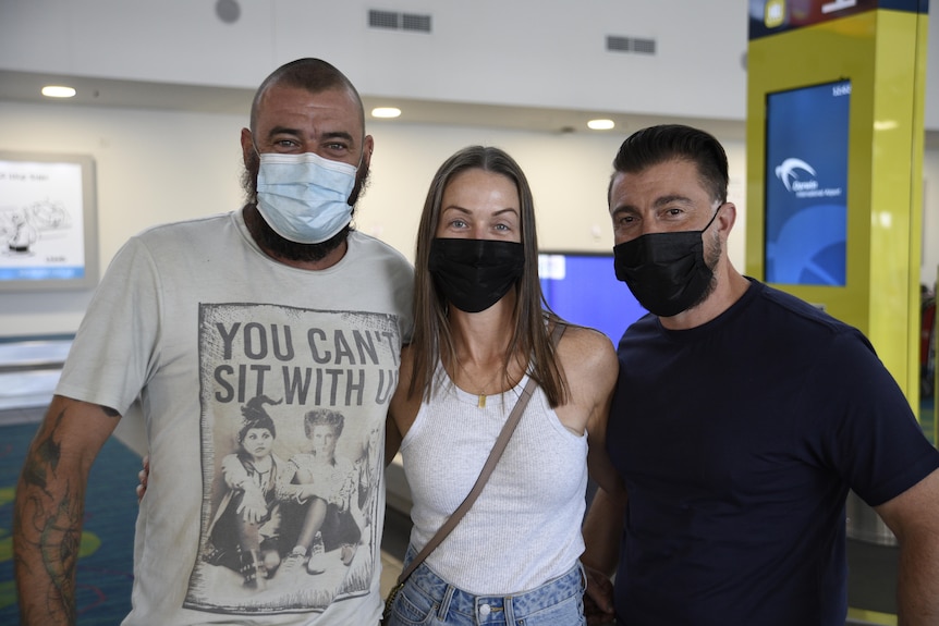 Two men and a woman wear masks in the airport.