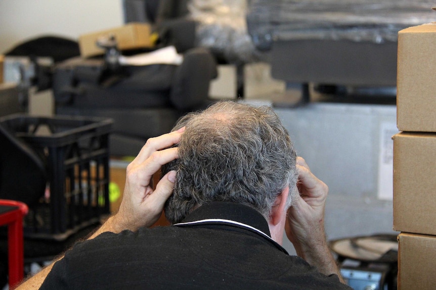 Balding man rubs the back of his head, looking stressed.