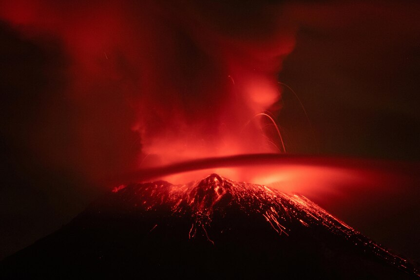 A plume of ash from a volcano is lit up in bright red at night.
