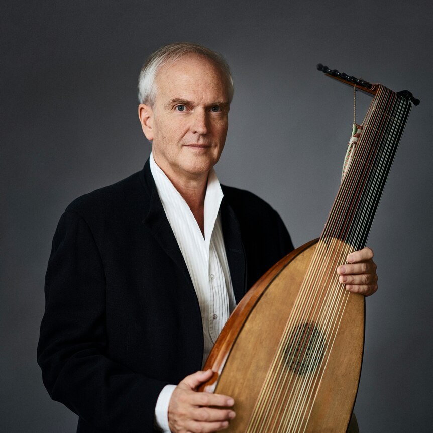 A man in a white shirt and black jacket holds a lute.