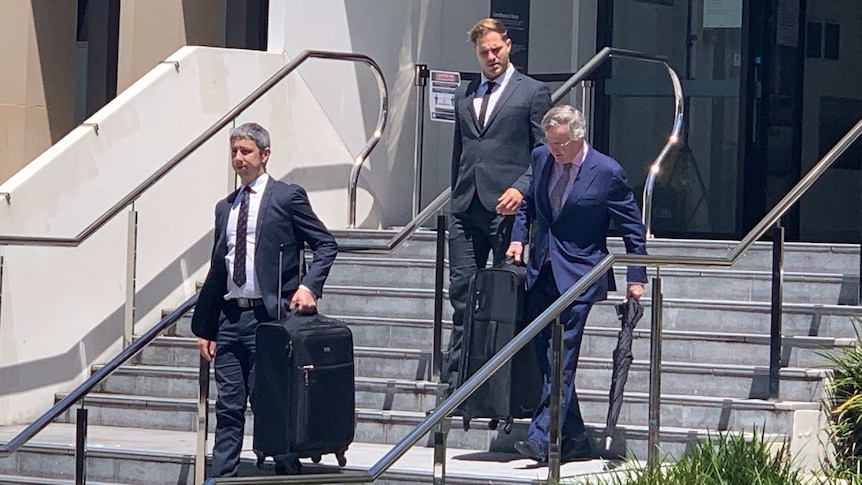 Three men in suits walk down stairs.