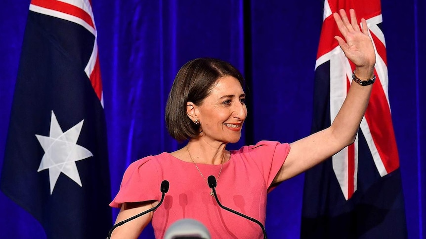 A female politician waving in front of Australian flags.