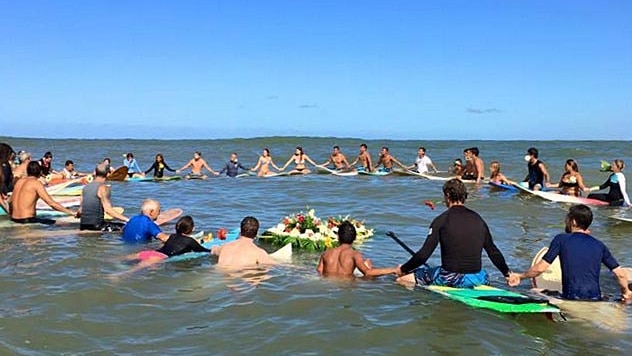 Surfers sit on their boards off the coast of Mexico and link hands during a paddle-out ceremony.