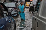 Indian woman in a sari walks in flooded street between cars.